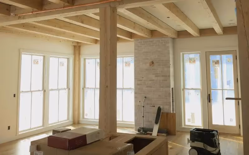 Unfinished interior with wooden beams, large windows, and exposed brick fireplace