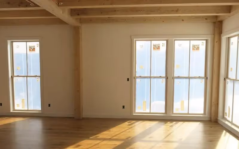Empty room with wooden floor, exposed beams, and large windows