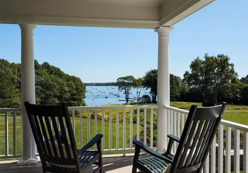 Two rocking chairs on porch overlooking peaceful harbor with boats