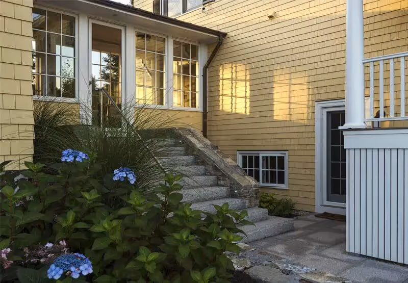 Yellow house with stone steps and blue hydrangeas in sunny afternoon light