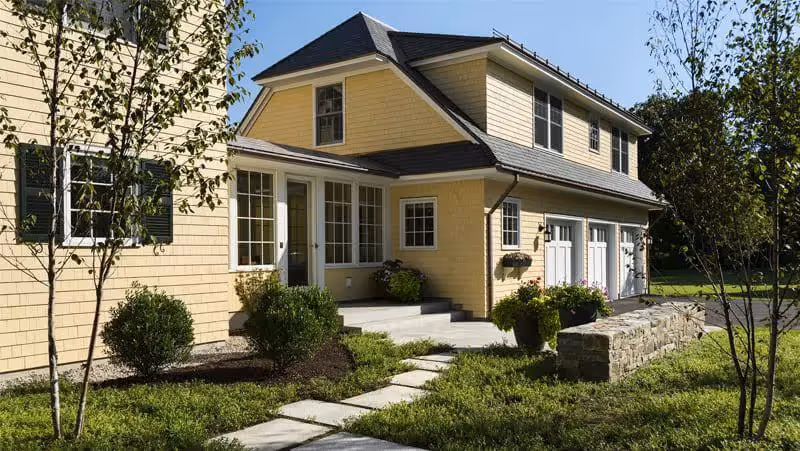 Yellow two-story house with stone pathway and well-maintained landscaping
