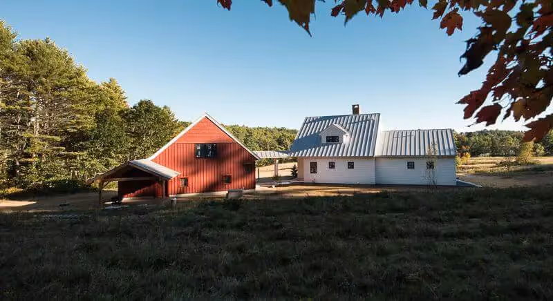 Red barn and white farm buildings on sunny day with autumn leaves