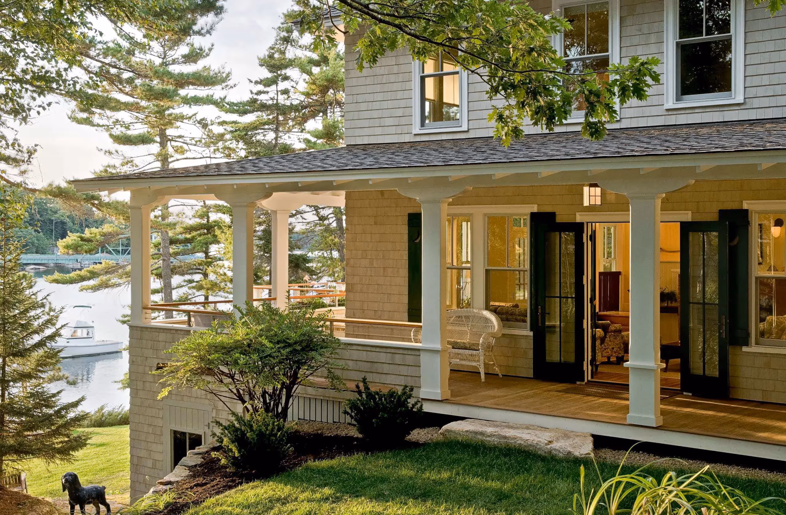 Coastal home with white porch, green trees, and boat in background