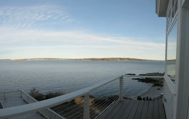 Coastal deck overlooking calm water with distant shoreline under cloudy sky