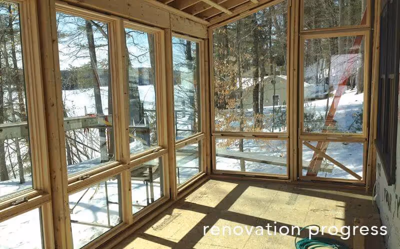 Wooden-framed sunroom with large windows overlooking snowy winter landscape