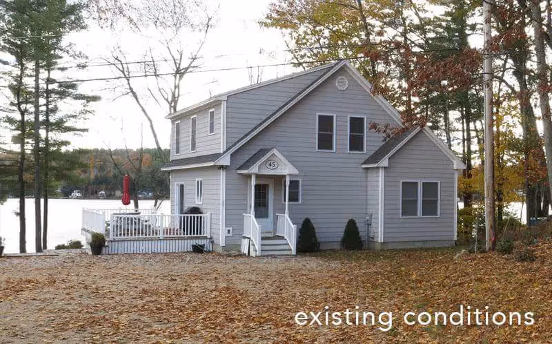 Gray two-story house near lake with white deck, surrounded by autumn trees