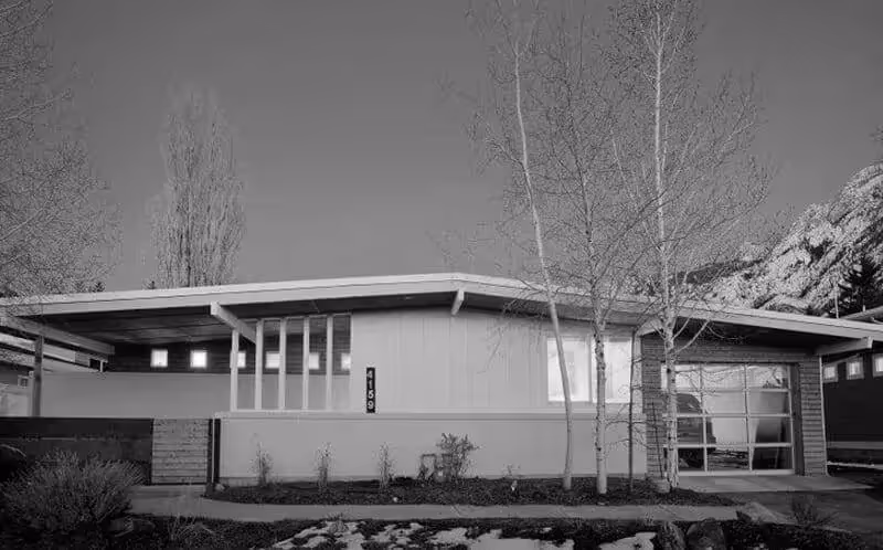 Mid-century modern house with large windows, set against trees and rocky mountain