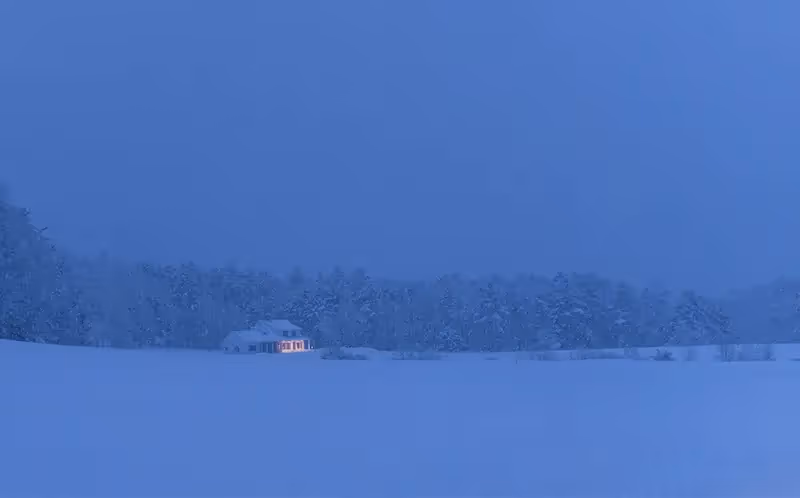 Lone house glows warmly in snowy winter landscape at dusk
