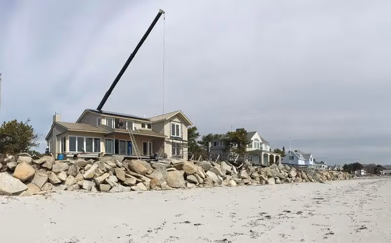 Beach houses with large crane, rocky shoreline, and storm damage protection