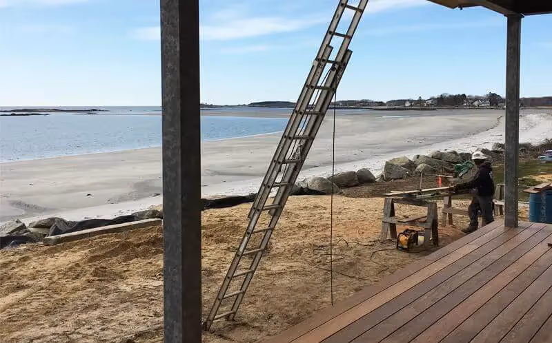 Construction site on sandy beach with ladder and worker near coastline