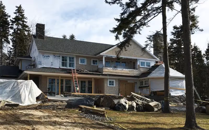Two-story house under construction with Tyvek wrap and surrounded by trees