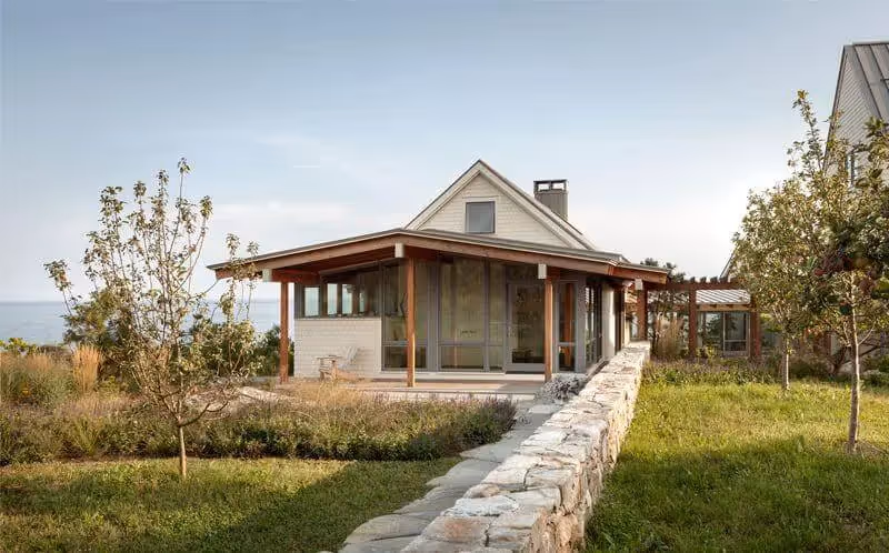 Modern coastal cottage with stone wall, wooden porch, and ocean view