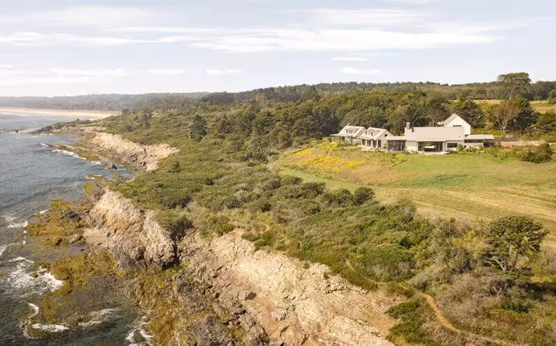 Coastal landscape with rocky shoreline, green vegetation, and white houses