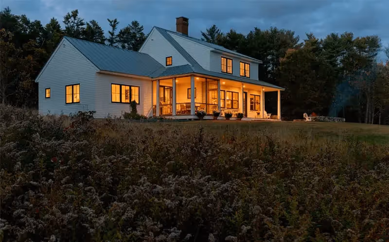 Warm-lit wooden house nestled in forest at dusk with glowing windows
