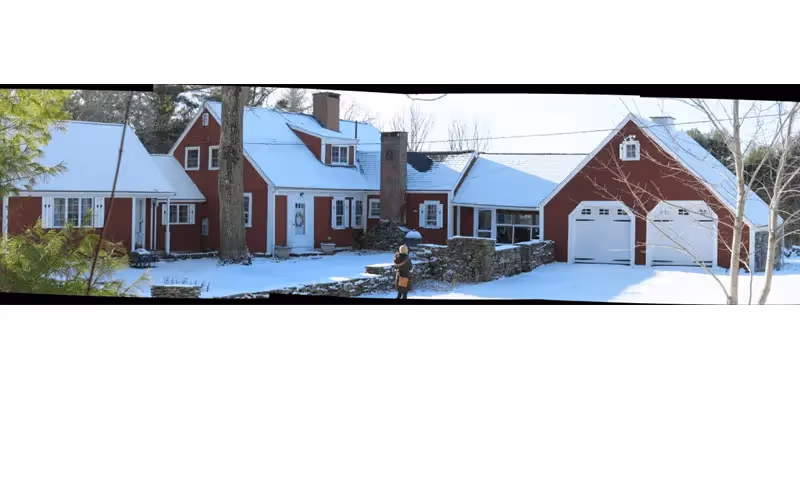 Red and white snowy house with two-car garage and stone wall in winter