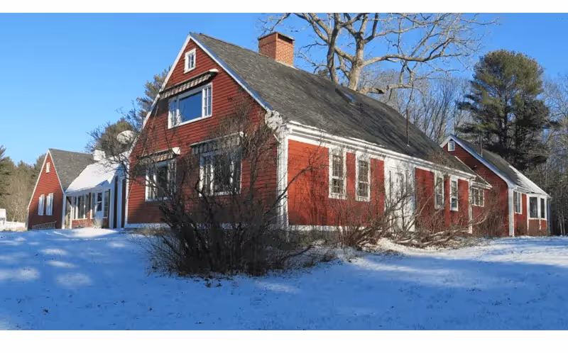 Red wooden house in snowy winter landscape with bare trees