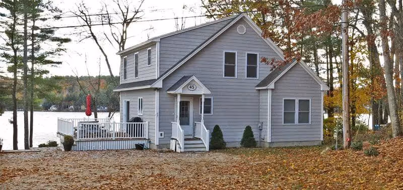 Gray lakeside cottage with white deck, surrounded by autumn trees