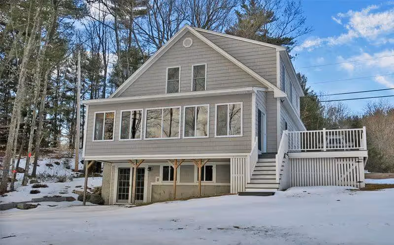 Two-story gray house with large windows in snowy winter woodland setting