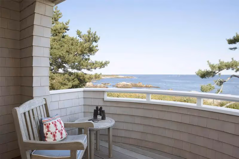 Coastal balcony with wooden chair, ocean view, and binoculars on table