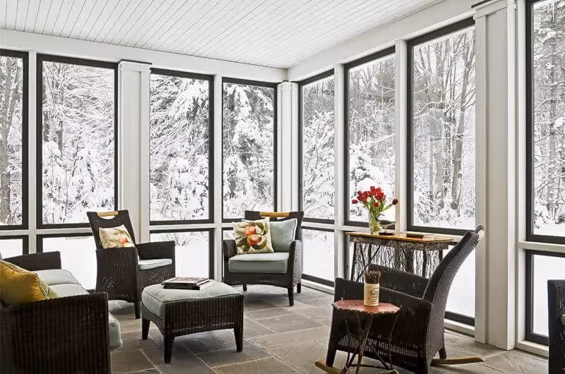 Cozy sunroom with wicker furniture overlooking snowy winter forest landscape