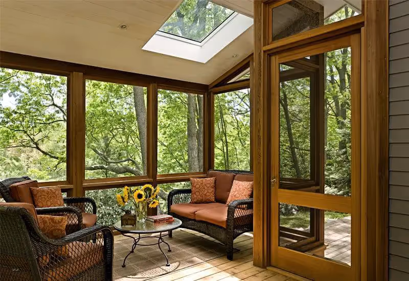 Sunlit screened porch with wicker furniture and sunflowers overlooking forest