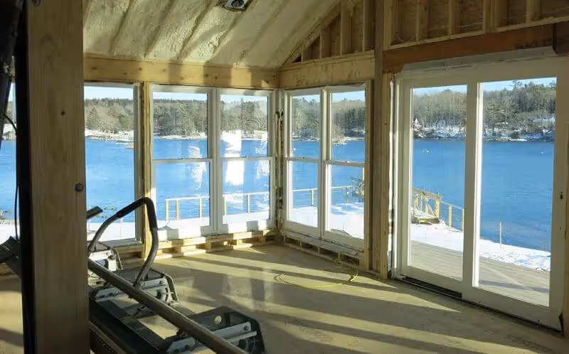 Wooden sunroom with large windows overlooking snowy lake and forest