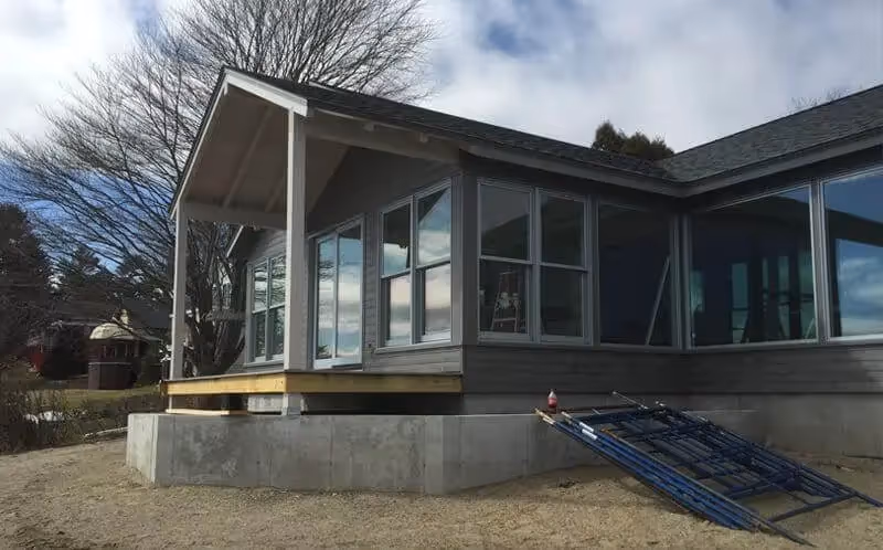 Modern house with large windows on concrete foundation, bare trees in background