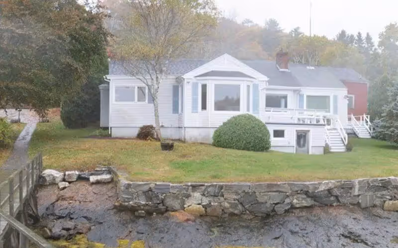 White house with stone wall, green lawn, and trees on misty autumn day
