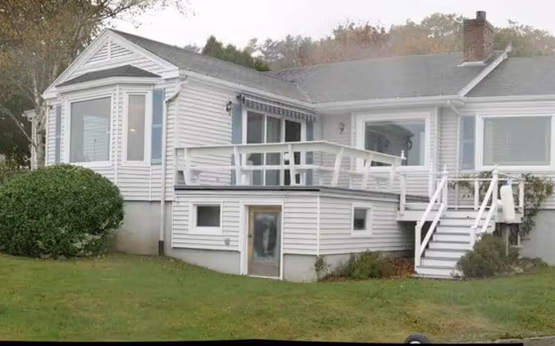 White two-story beach house with deck and green lawn in autumn