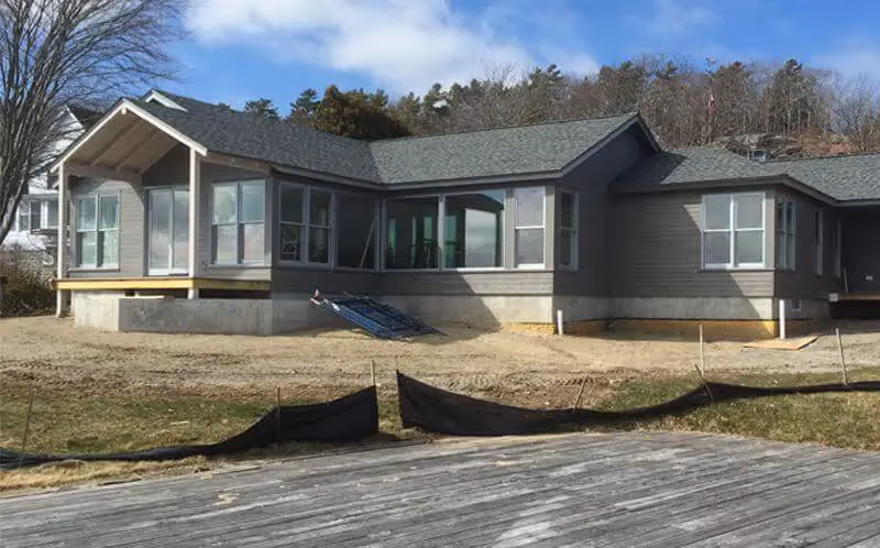 Modern gray house under construction with large windows and wooden deck
