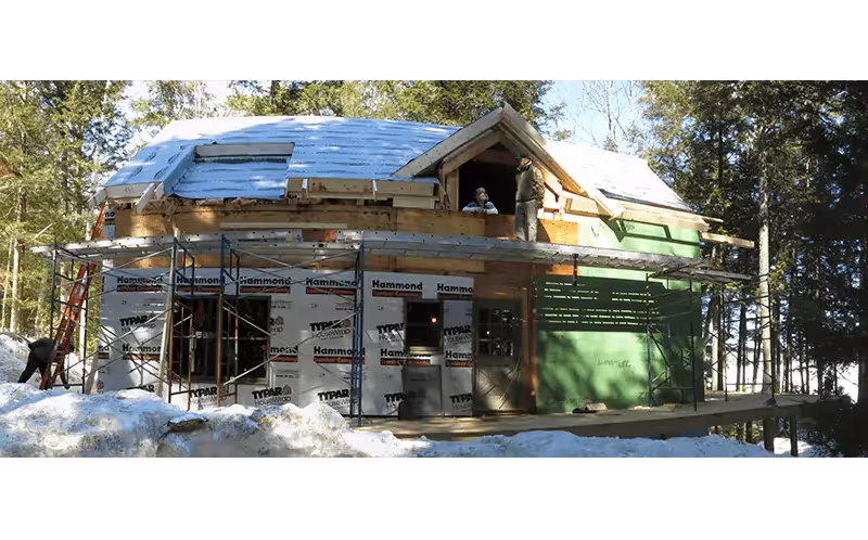 Wooden cabin under construction in snowy forest with scaffolding