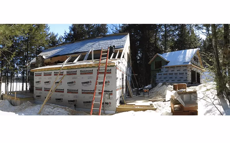 House under construction in snowy wooded area with ladders and building materials