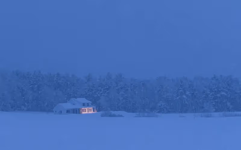 Warm glowing cabin nestled in snowy forest during blue winter twilight