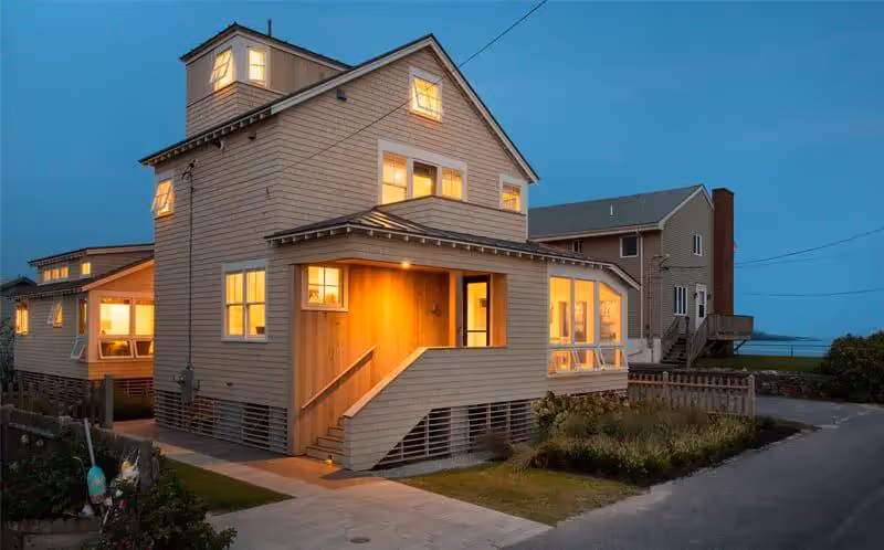 Warm glowing beach house at dusk with windows illuminated