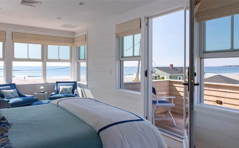 Coastal bedroom with ocean view, blue chairs, and white bedding