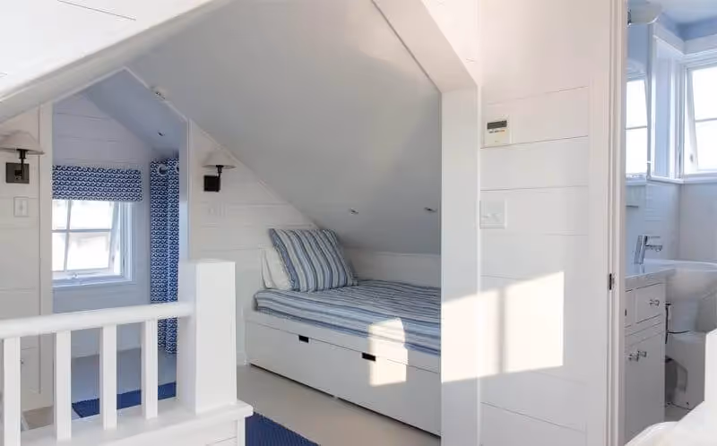 Cozy attic bedroom with white walls, built-in bed, and blue accents
