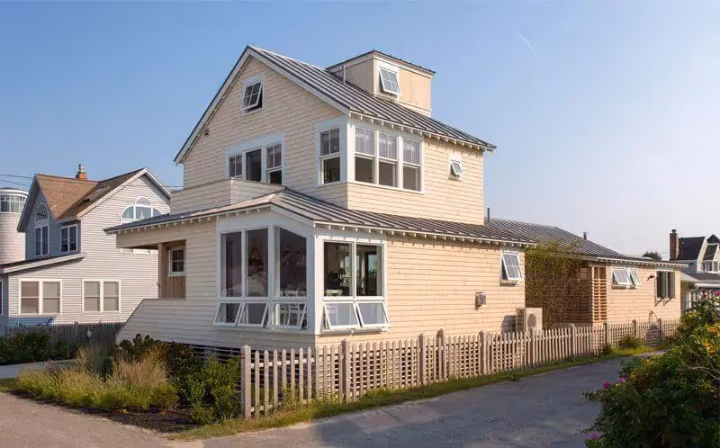 Yellow beach house with white trim and picket fence on sunny day