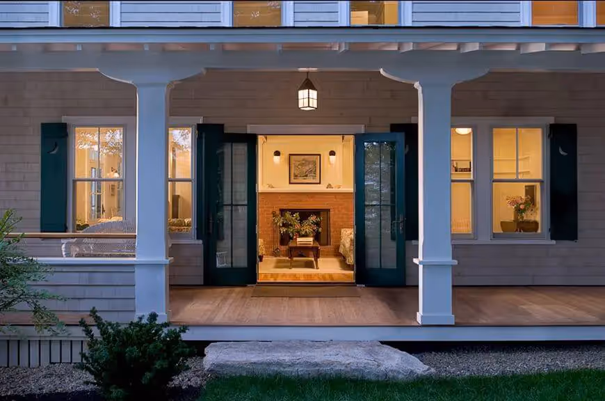 Cozy home exterior with warm lighting, open doors, and brick fireplace at dusk