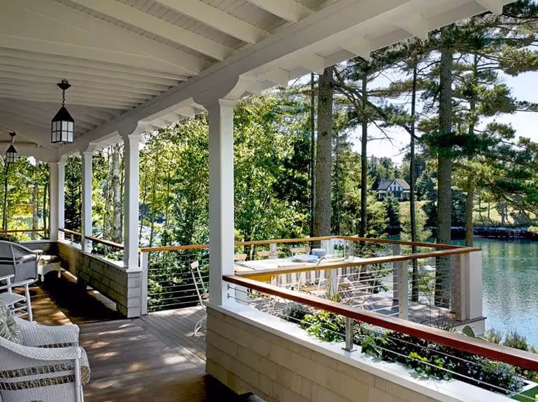 Wooden porch overlooking lake with white railing and lush green trees