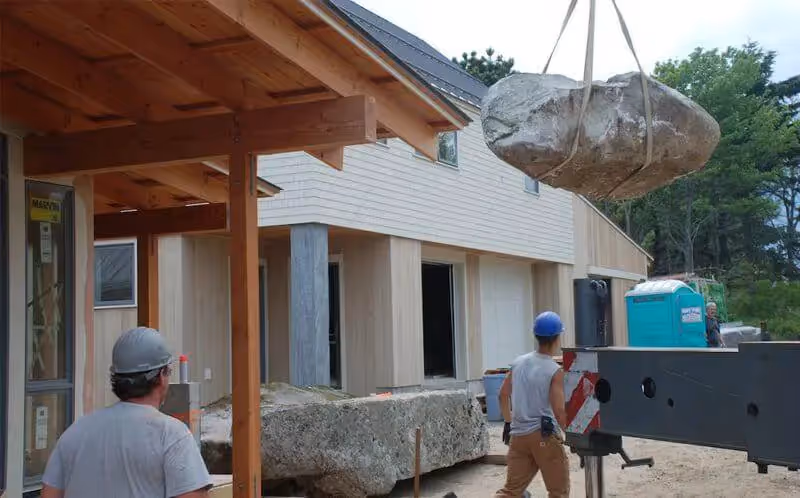 Construction workers using crane to move large boulder at building site
