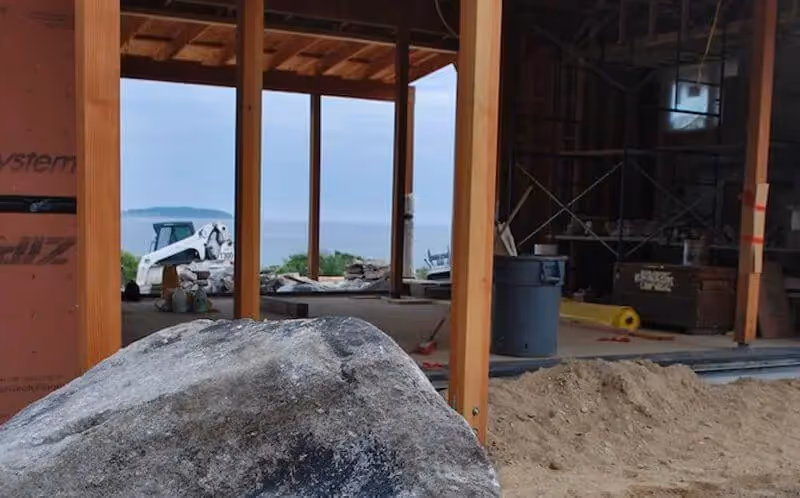 Construction site with wooden frame, rock, and view of water and equipment