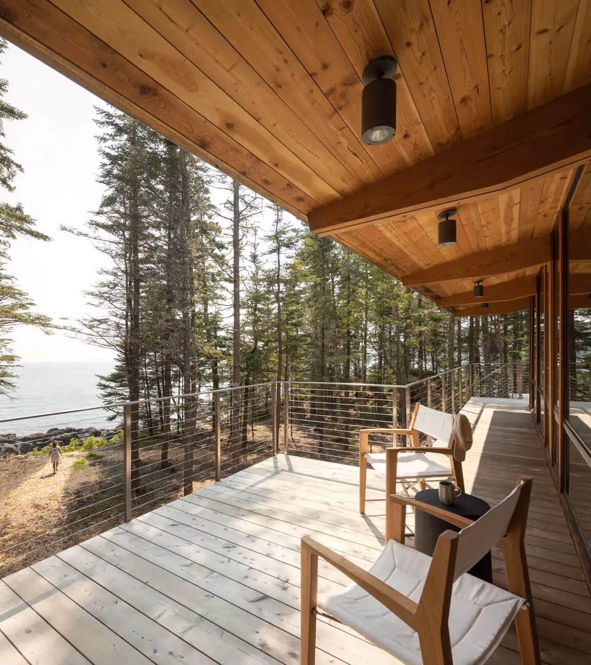 Wooden deck overlooking forest and ocean with modern chairs
