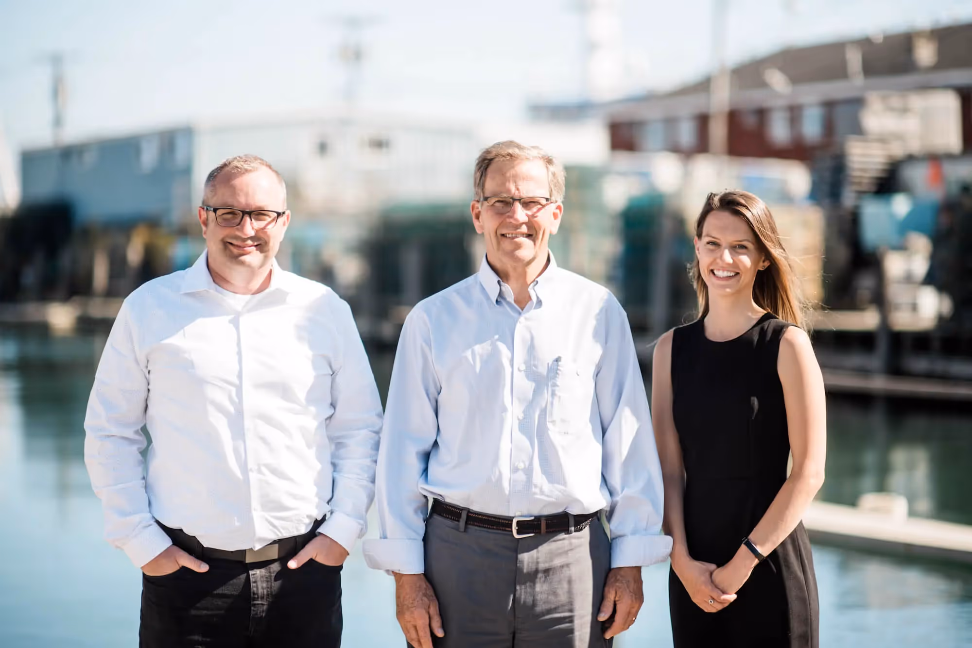 Three professionals smiling together near waterfront with urban buildings