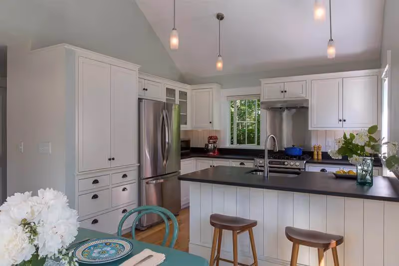 Modern white kitchen with island, pendant lights, and wooden bar stools