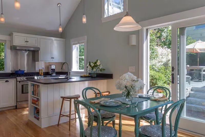 Bright kitchen with white cabinets, green dining table, and garden view