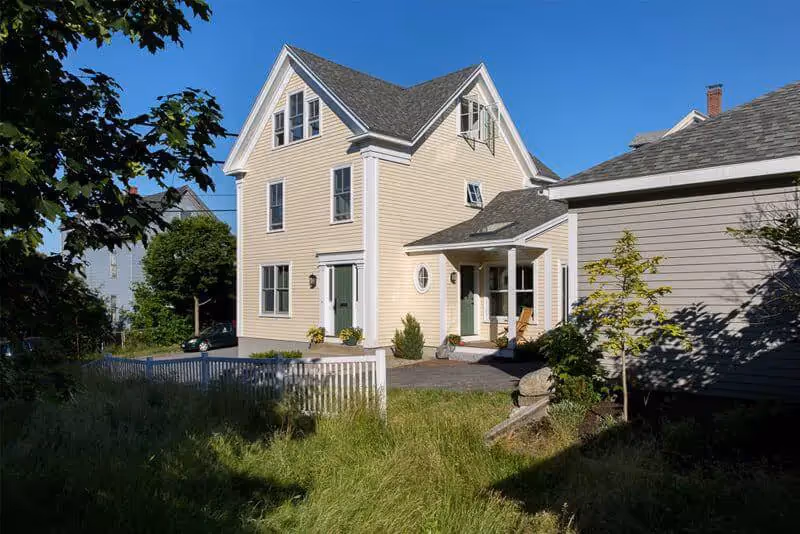 Yellow coastal house with green door and white fence on sunny day