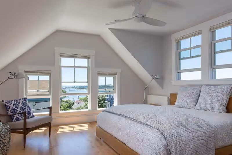 Bright attic bedroom with ocean view, wood floor, and blue decorative pillow