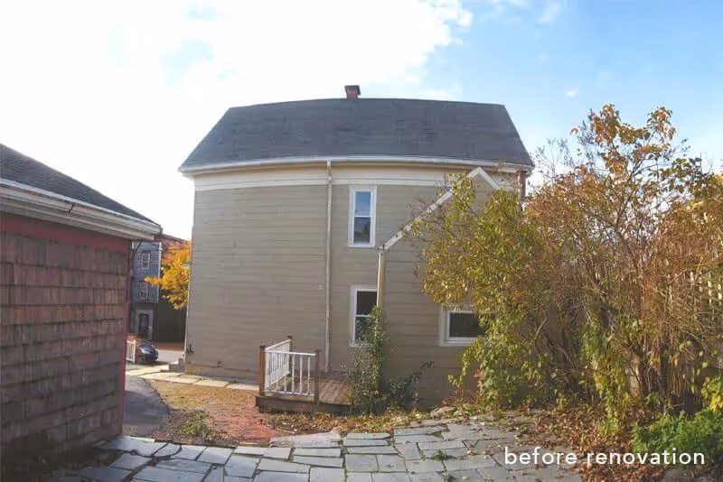 Old two-story house with white siding before renovation, autumn trees nearby