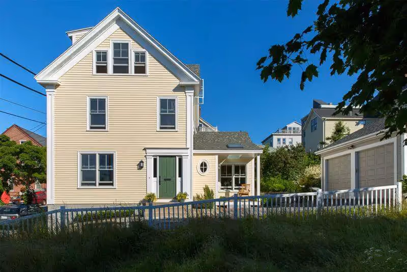 Yellow coastal home with green door and white fence on sunny day