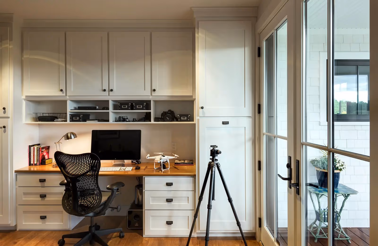 Home office with white cabinets, wooden desk, camera equipment, and drone